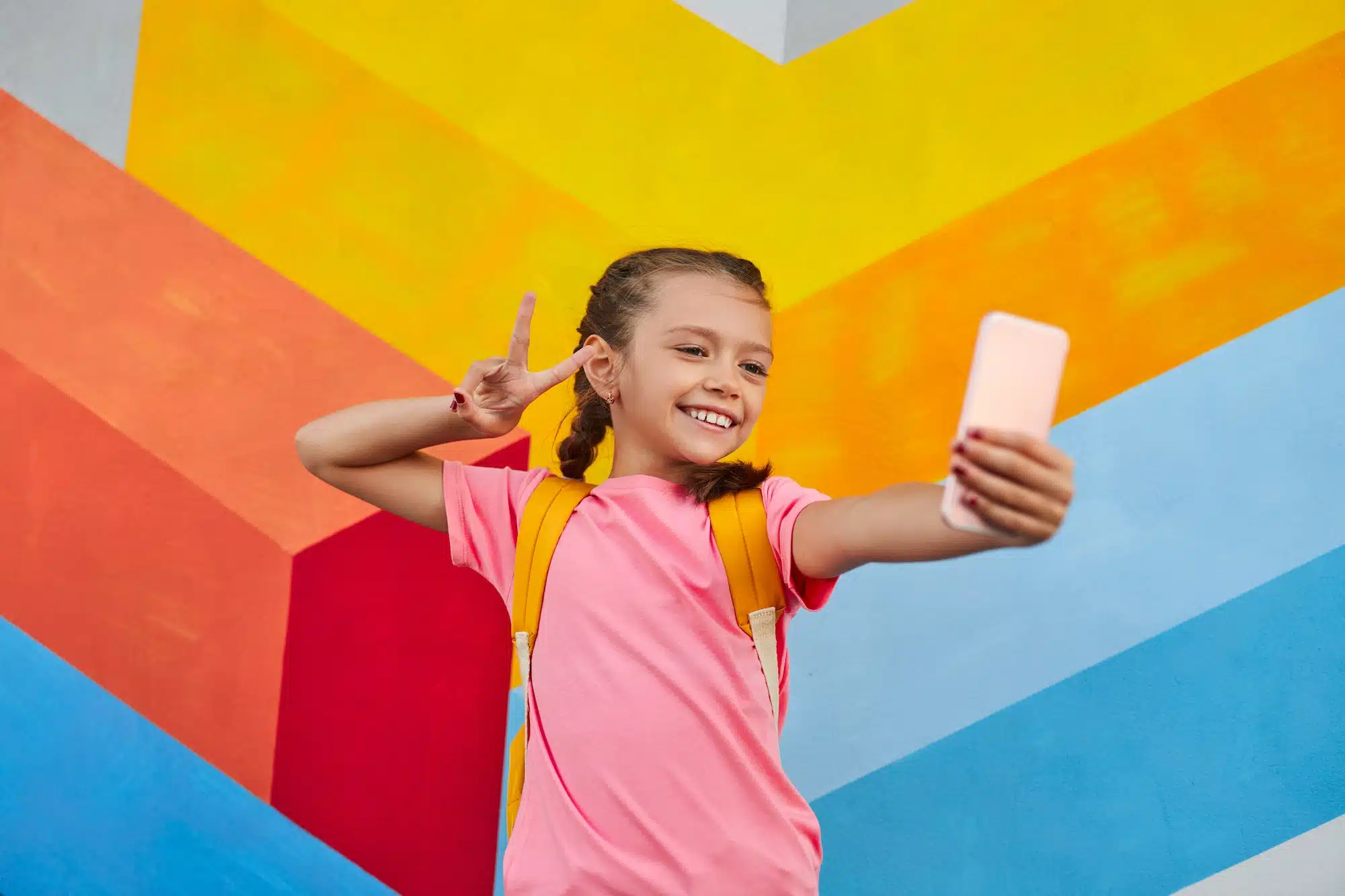 Positive schoolgirl taking selfie on smartphone