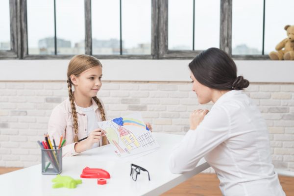 little-blonde-girl-showing-drawn-house-on-paper-to-her-female-psychologist little-blonde-girl-showing-drawn-house-on-paper-to-her-female-psychologist